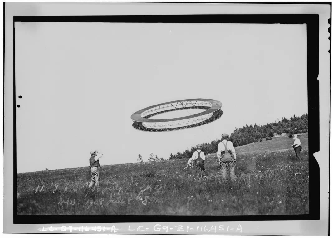 A circular tetrahedral kite flying above four people in a field
